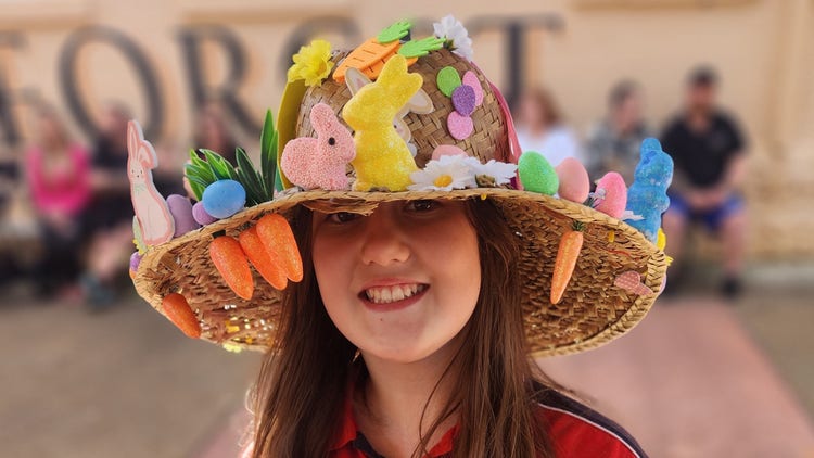 A student wearing a wide-brimmed hat decorated with bunnies, eggs, and carrots.