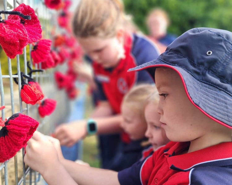 Students tying crochet poppies to the school fence.